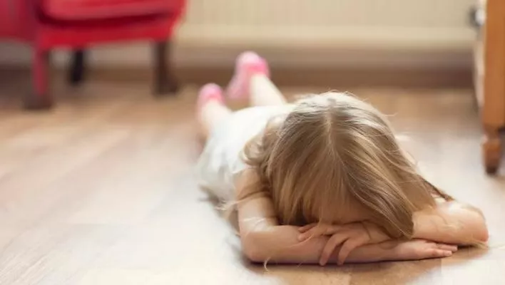 A frustrated child lying on the floor, displaying signs of distress and frustration. The child's body language indicates sadness and dissatisfaction. The image represents the negative effects that can arise from keeping a child away from the other parent