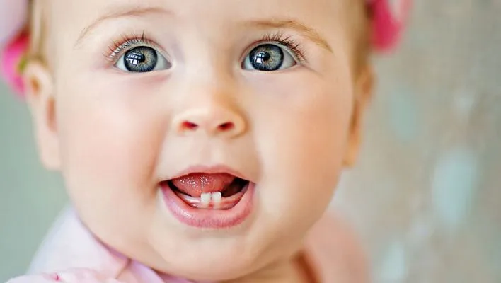 A surprised child with wide eyes, debunking misunderstandings surrounding delayed teething as a measure of intelligence.  